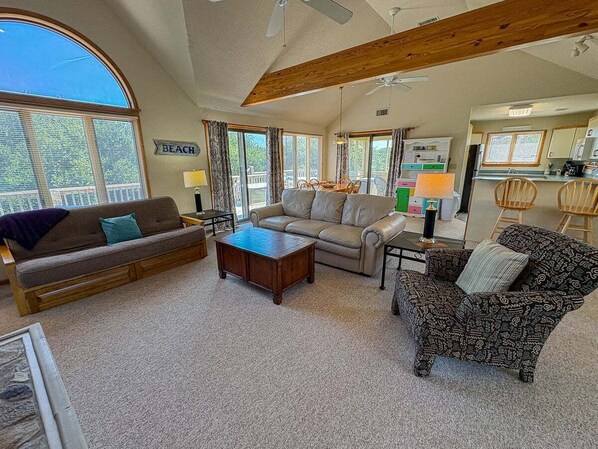 A spacious living room with a large window, a sofa, a patterned armchair, and a coffee table.