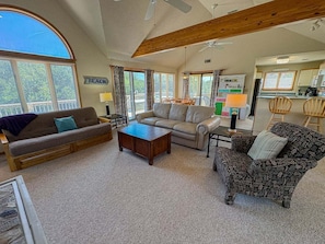 A spacious living room with a large window, a sofa, a patterned armchair, and a coffee table.