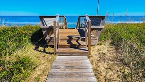 Une promenade en bois mène à une plage, avec une structure en bois visible en arrière-plan.