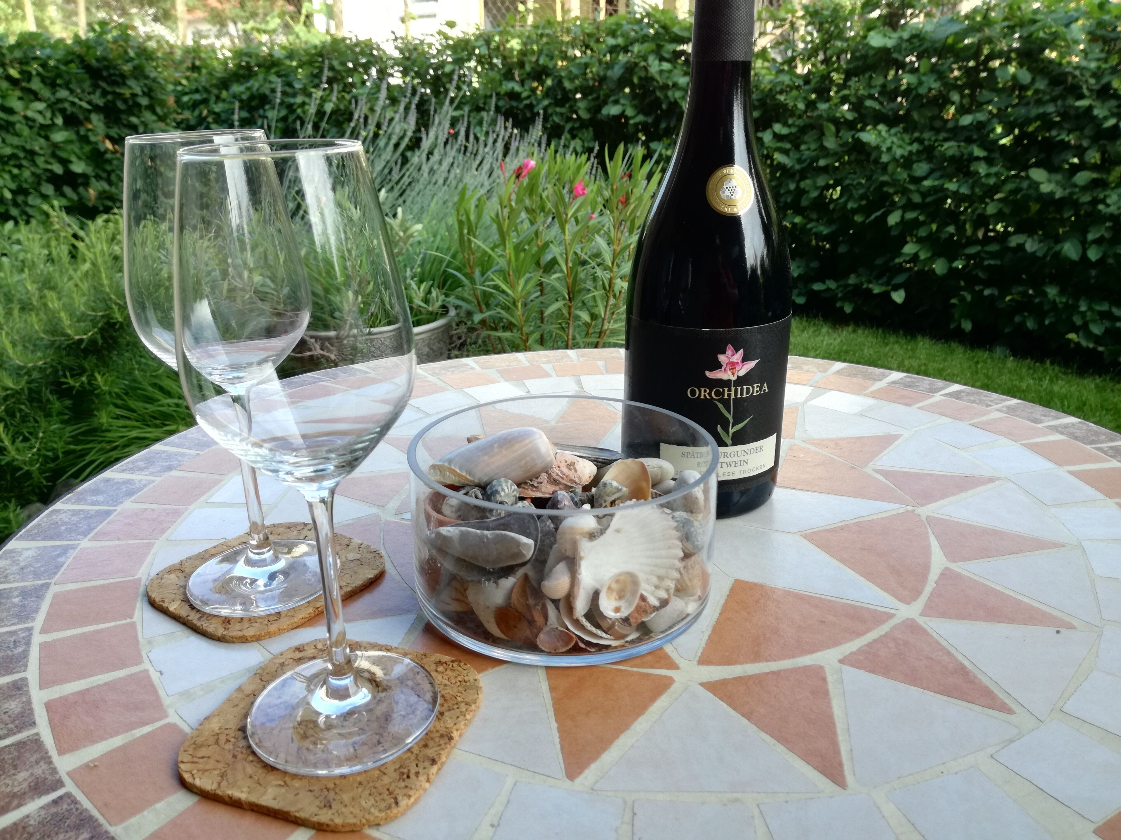Een tafel met drie wijnglazen, een fles wijn en een schaal schelpen.