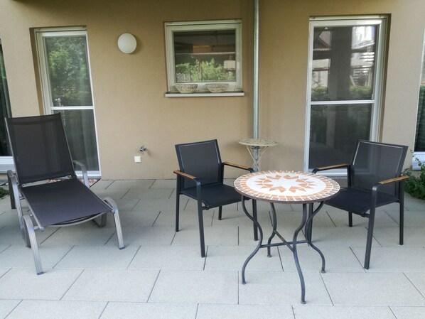 Una terrazza esterna con quattro sedie e un tavolino rotondo, circondata da ampie finestre.