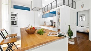 Une cuisine moderne avec des meubles blancs, un îlot central en bois et un coin repas avec des chaises.
