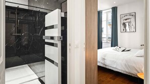 Une chambre d’hôtel moderne dotée d’une douche en verre, d’un lit avec une literie blanche et d’un mur décoratif en bois.