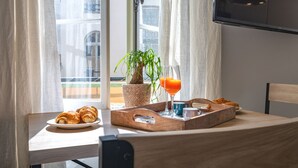 Un plateau de petit-déjeuner avec des croissants, une plante et du jus d’orange, posé sur une table près d’une fenêtre ornée de rideaux.