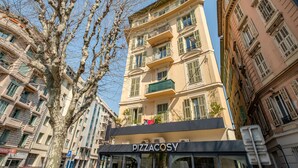 Un immeuble à plusieurs étages dont la devanture porte l’inscription « PIZZACOSY ».