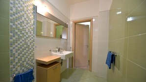 Ein Badezimmer mit gefliestem Boden, einem Waschbecken mit Spiegel darüber, einem Holzkästen und einem Handtuch an der Wand.