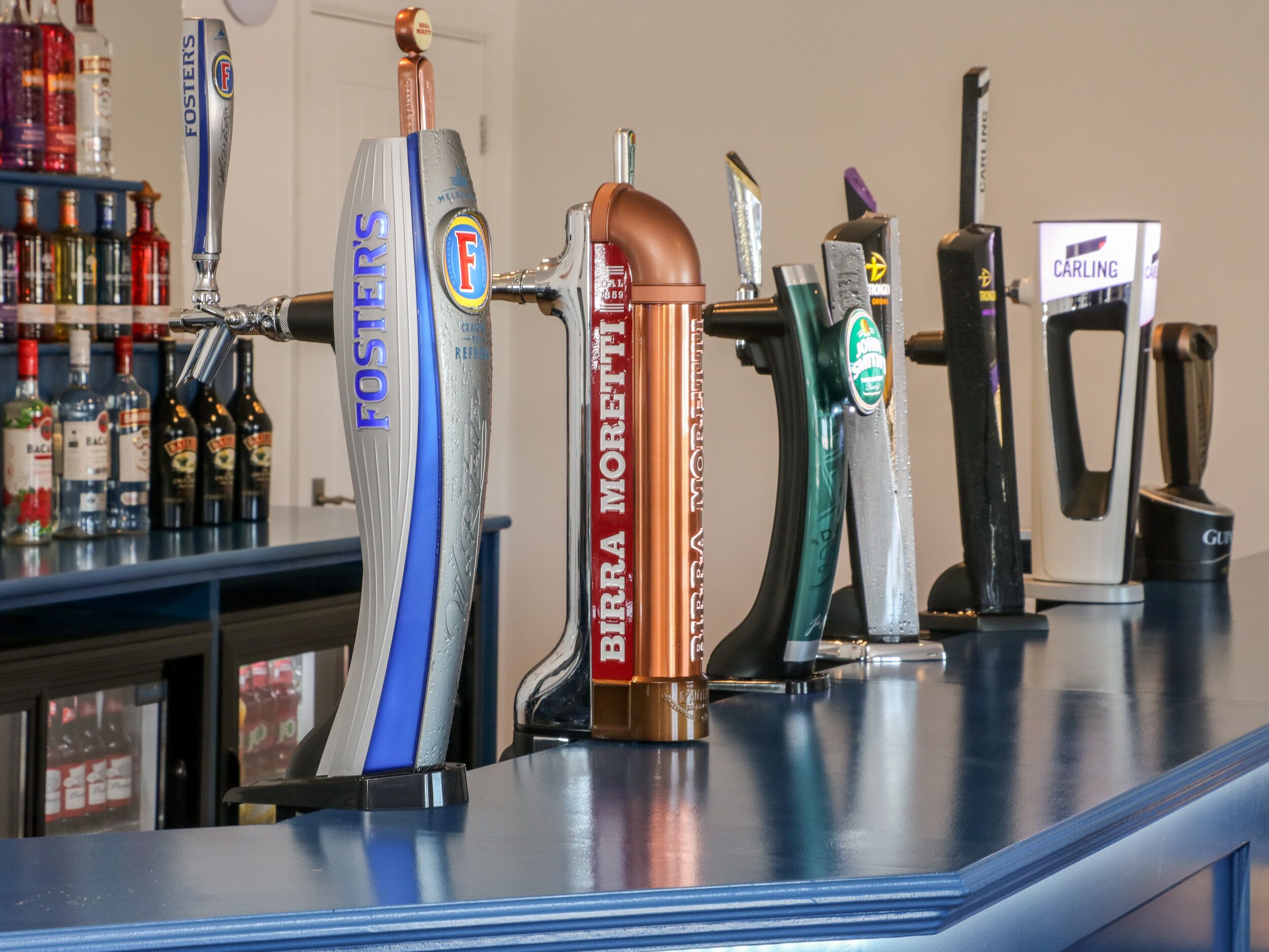 A bar counter with various tap handles, including brands like Foster's and Birra Moretti.