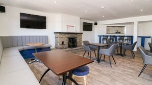A modern lounge area with a stone fireplace, a flat-screen TV, and a bar area. - Chalet 1 (Malton)