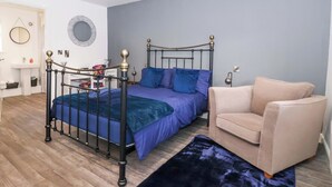 A bedroom with a bed, a chair, a bedside table, a mirror, and a wall-mounted light fixture. - Chalet 1 (Malton)