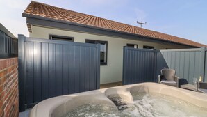 A hot tub with a brick wall and a blue fence in a backyard. - Chalet 1 (Malton)