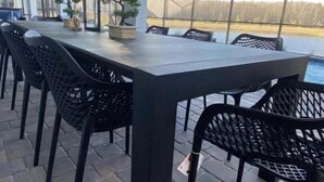 Un patio al aire libre con una mesa larga y sillas, un cerramiento de vidrio y vista a un cuerpo de agua.