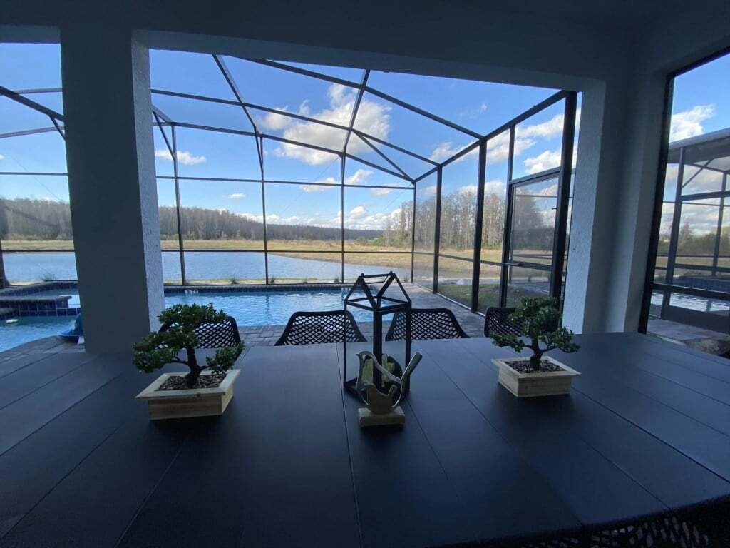 Une pièce dotée d’une grande fenêtre donnant sur un plan d’eau et une piscine. Une table est ornée de trois plantes en pot.