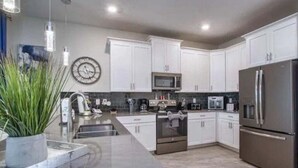 Una cocina moderna con armarios blancos, electrodomésticos de acero inoxidable y un reloj en la pared.