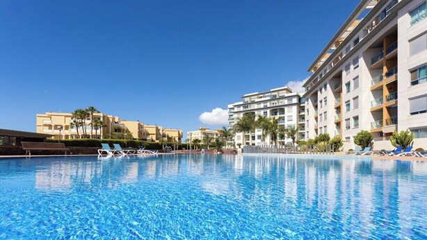 Una piscina con sillas de descanso, rodeada de edificios de varios pisos con balcones.