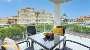 Un balcón con sillas de mimbre, una mesa de vidrio con fruta y vistas a un edificio de hotel.