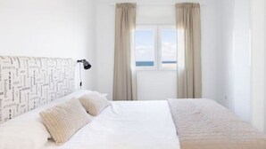 A hotel room with a bed, a window with curtains, a wall with a pattern, and a nightstand with a lamp. - Home2Book Serene Apartment Ocean Breeze, Bajamar (Bajamar)