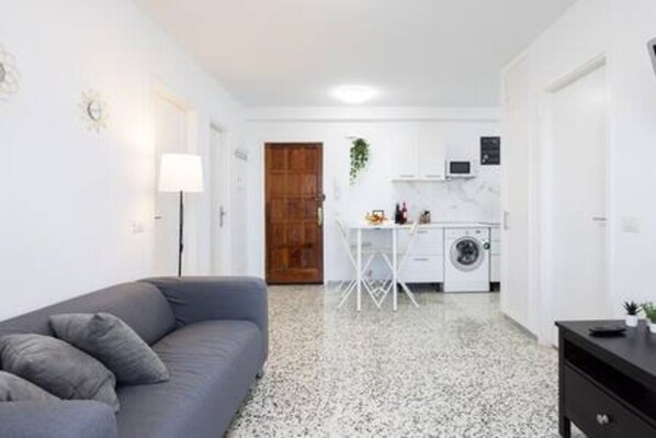 A compact living space with a grey sofa, a small table, a washing machine, and a white cabinet.