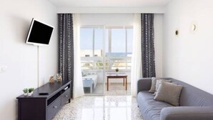 A modern living room with a grey sofa, a flat-screen TV mounted on the wall, a small table, and a view of the outdoors through a glass door. - Home2Book Serene Apartment Ocean Breeze, Bajamar (Bajamar)
