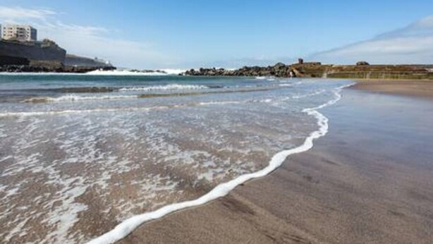 A beach with waves lapping onto the shore, a rocky outcrop in the background, and buildings on the far side. - Home2Book Serene Apartment Ocean Breeze, Bajamar (Bajamar)