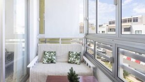 A balcony with a cushioned seating area, large windows, and a view of buildings. - Home2Book Serene Apartment Ocean Breeze, Bajamar (Bajamar)