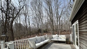 Una terraza de madera con barandilla blanca, alfombra gris y sofá blanco con almohadones a rayas.