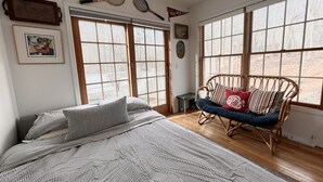 Un dormitorio con una cama grande, una silla de mimbre y varios ventanales.