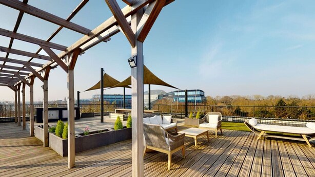 Terraza en la azotea con suelo de madera, mobiliario exterior y vistas a un edificio moderno.