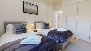 Habitación de hotel con dos camas, una mesita de noche con lámpara, un armario y un cuadro en la pared.
