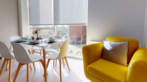 Un comedor con una mesa lista para cuatro personas, sillas y una ventana con persianas.