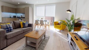 Una sala de estar moderna con un sofá, una mesa de centro y un sillón amarillo. Hay un comedor con sillas y una mesa, y una cocina con armarios y electrodomésticos.