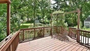 A wooden deck with a metal railing, surrounded by lush greenery and trees. - Cheerful residential house with all yours needs. (St. Louis)