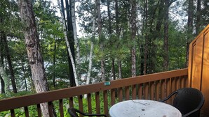 A wooden deck with a round table and two chairs, surrounded by tall trees. - Birch Point Resort Condo #19 - Nelson Lake, Hayward (Hayward)