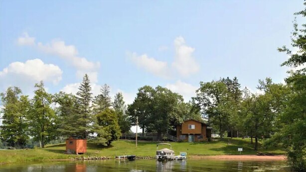 A lakeside view with a small cabin, a larger house, and boats on the water. - Birch Point Resort Condo #19 - Nelson Lake, Hayward (Hayward)