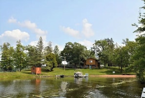 Escape to a serene lakeside retreat surrounded by lush greenery and trees, where a cabin and a house offer a tranquil atmosphere and opportunities for boating.