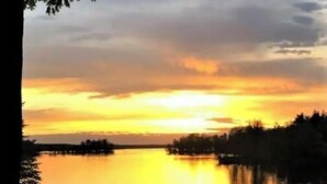 A calm lake at sunset with a dock and a boat.