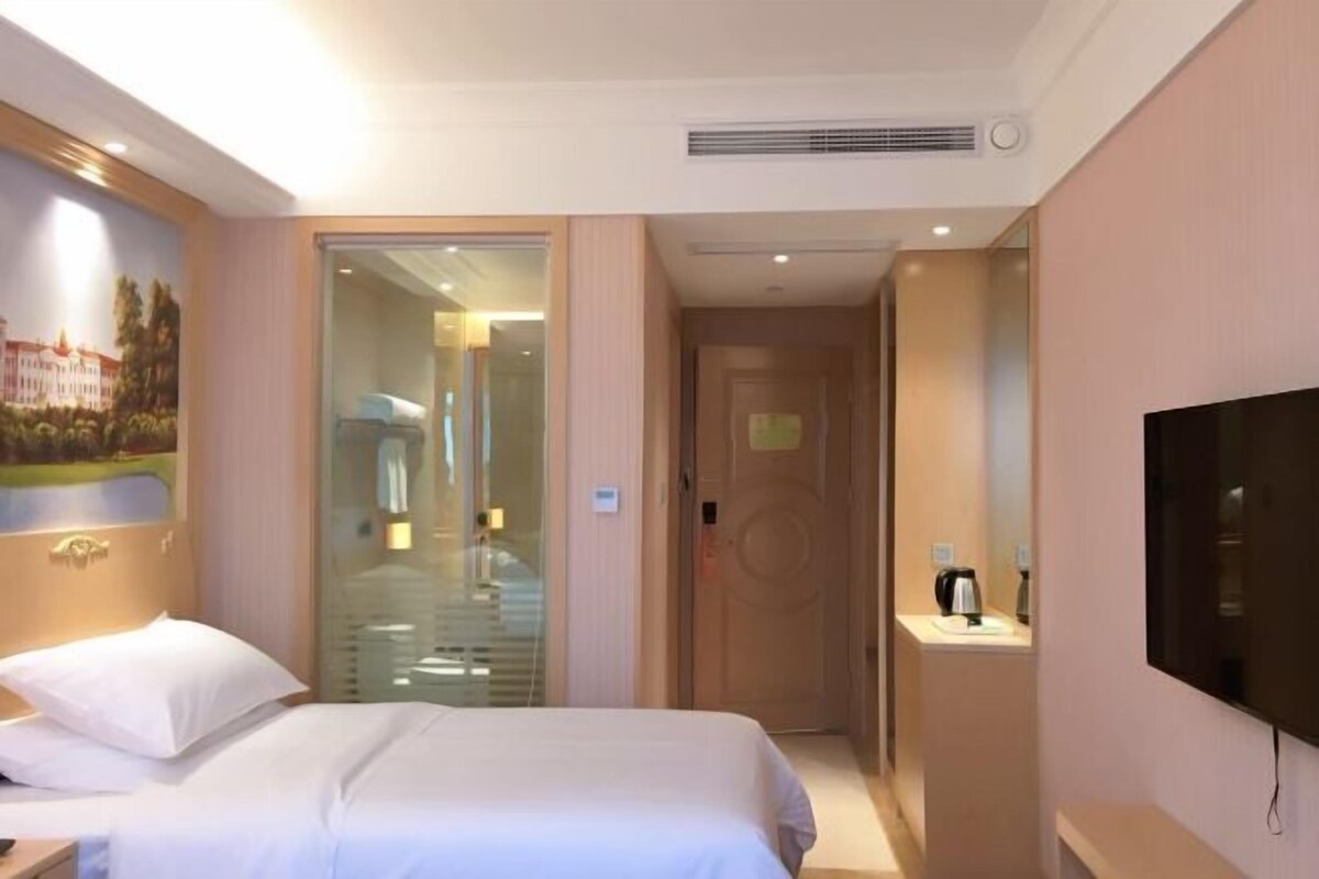 A hotel room with a bed, a television, a door, and a painting on the wall.