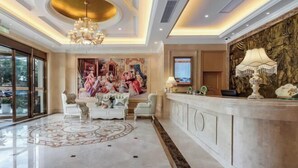 Un lobby lujoso con piso de mármol, un candelabro, un mostrador de recepción y un cuadro grande de una escena histórica.