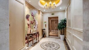Un pasillo con piso de mármol, una araña, un cuadro, una puerta y una planta en maceta.