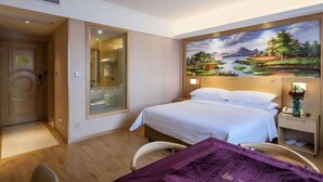 A hotel room with a bed, a nightstand, a mirror, and a painting of a landscape on the wall. - Vienna Hotel (Shanghai Hongmei South Road) (Shanghai)