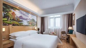 A hotel room with a large bed, a desk, a chair, a TV, and a painting on the wall. - Vienna Hotel (Shanghai Hongmei South Road) (Shanghai)