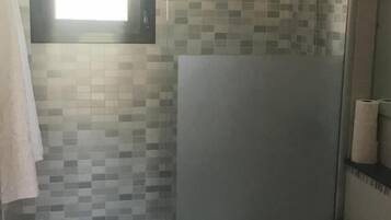 A bathroom with a glass shower enclosure, a toilet, and a sink.
