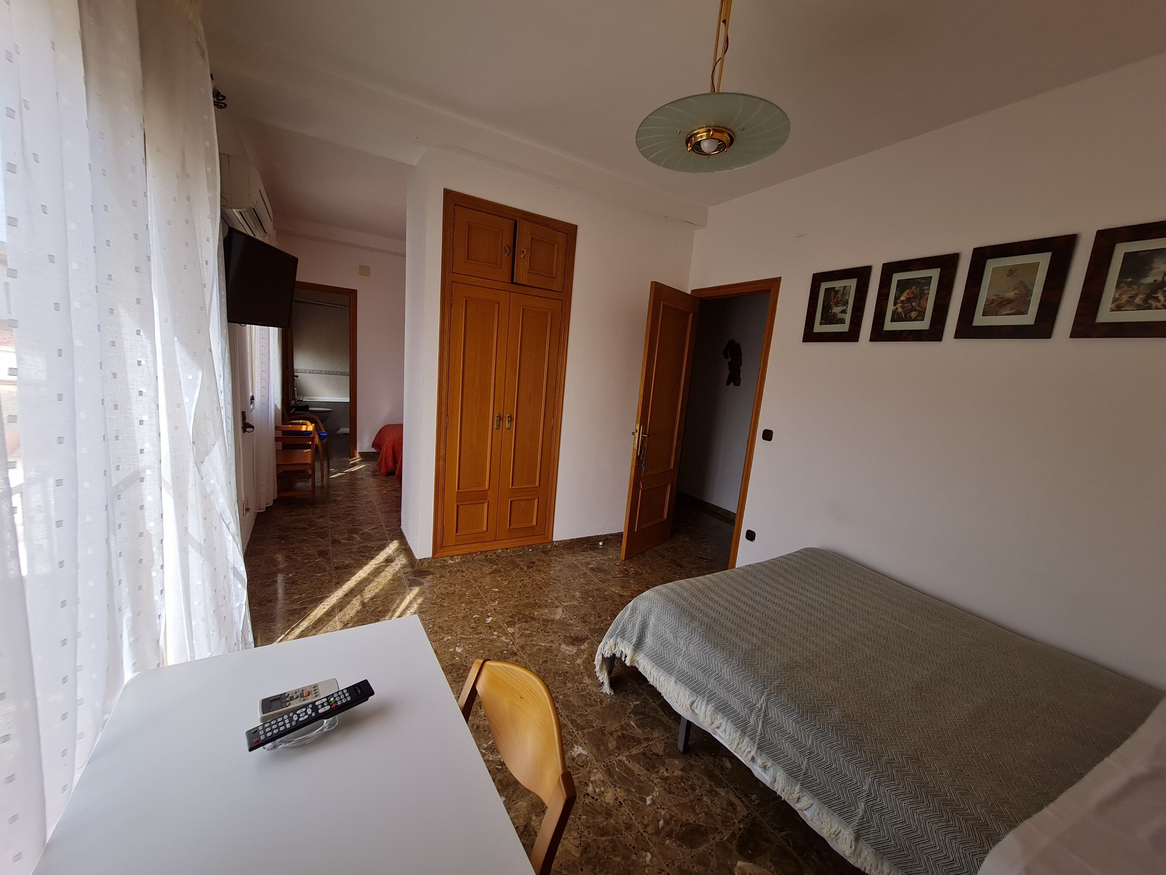 A bedroom with a bed, a desk with a remote control, a chair, and a wardrobe.