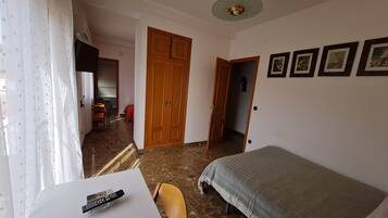 A bedroom with a bed, a desk with a remote control, a chair, and a wardrobe.