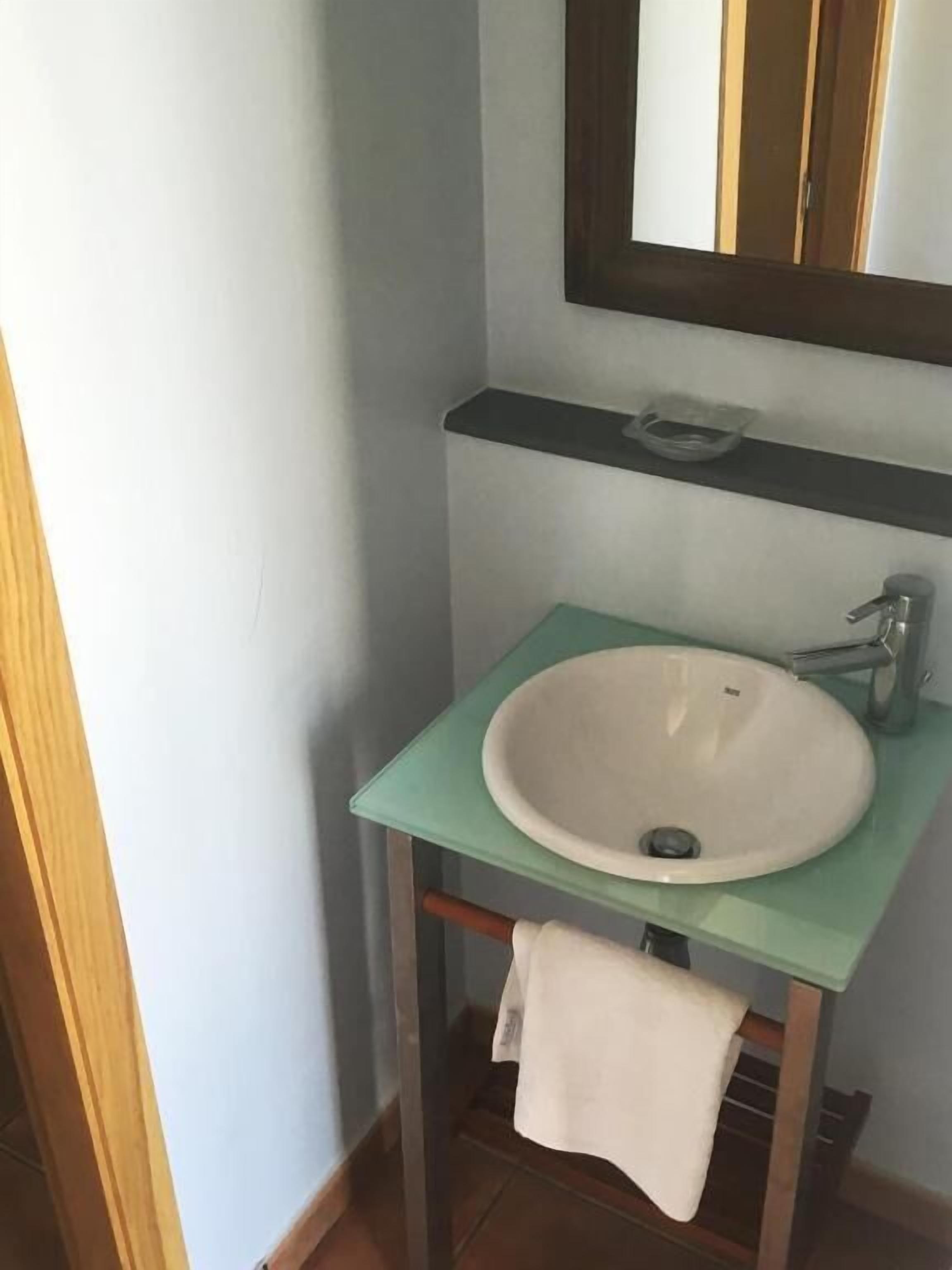 A bathroom with a white sink on a green countertop, a mirror above it, and a towel hanging on a rack.