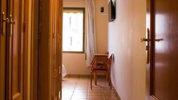 Un pasillo con puertas de madera, suelo de baldosas y una ventana con cortinas.