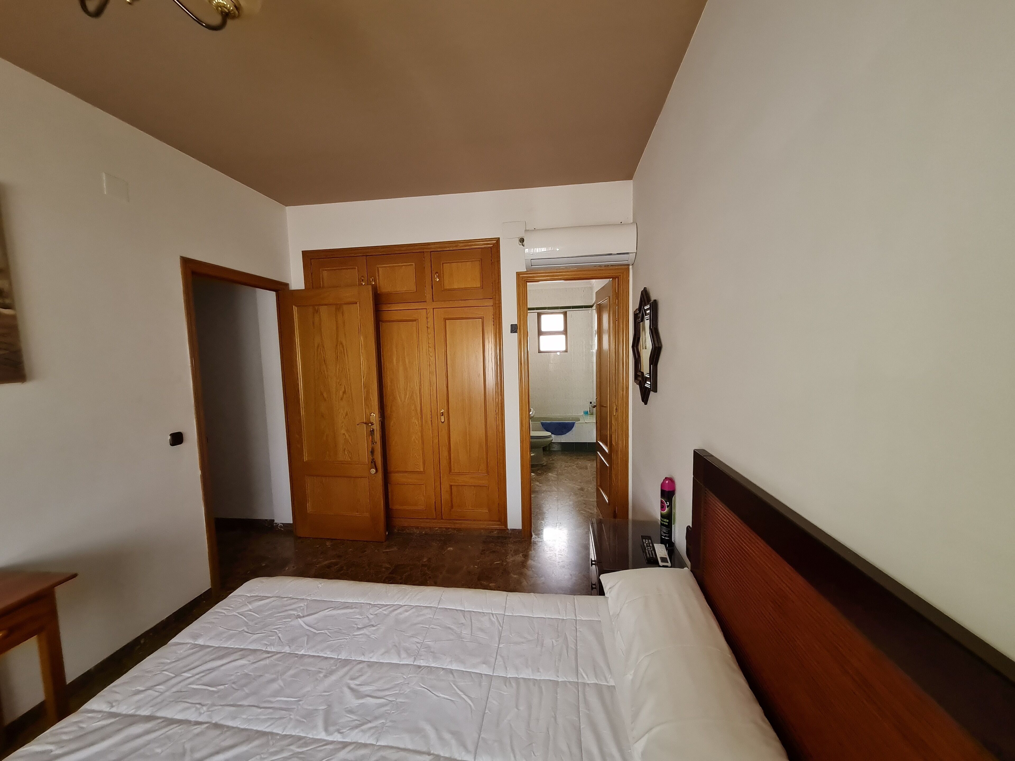 A bedroom with a bed, wooden wardrobe, and an air conditioning unit.