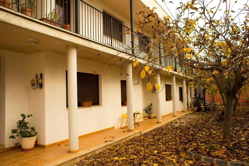 Un espacio al aire libre cubierto con columnas blancas, un balcón con barandillas negras y un árbol con hojas amarillas.