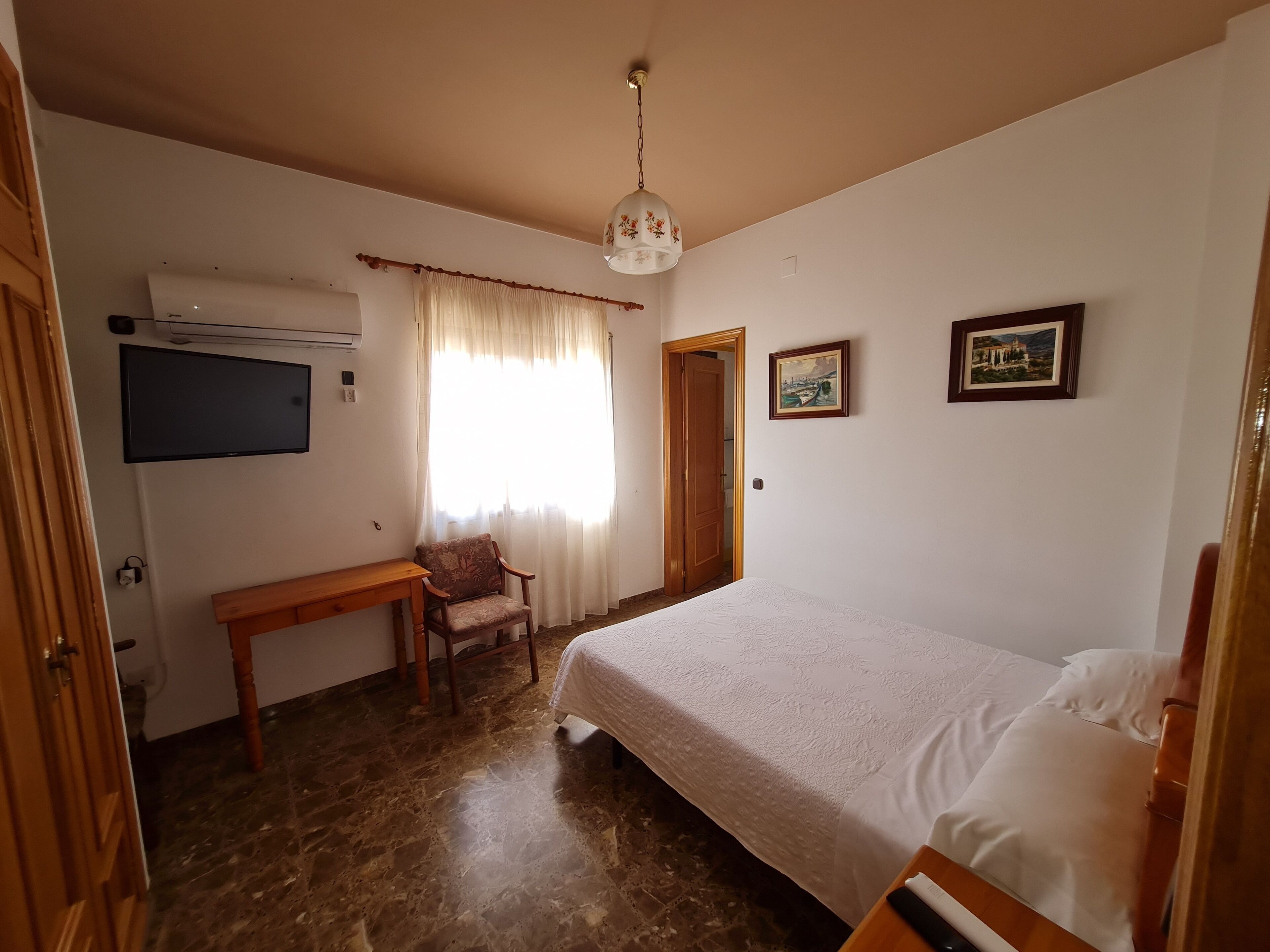 Un dormitorio con una cama, un escritorio, una silla, un aire acondicionado y dos cuadros en la pared.