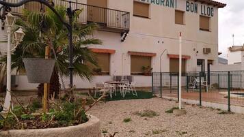 Ein Gebäude mit der Aufschrift „RESTAURANT BON LLOC“ und Außenbereich mit Sitzgelegenheiten und Blumentöpfen.