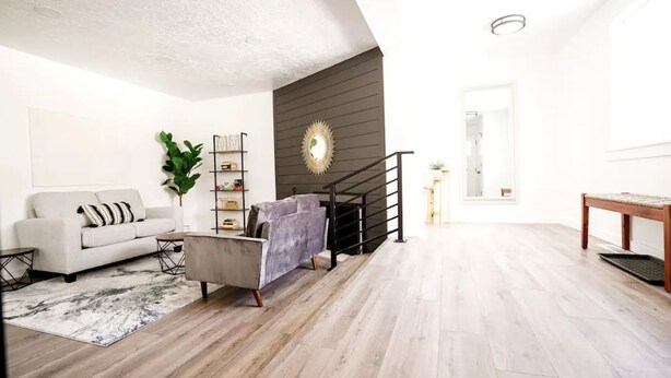Een moderne woonkamer met een bank, fauteuil en een trap die naar een hoger niveau leidt.